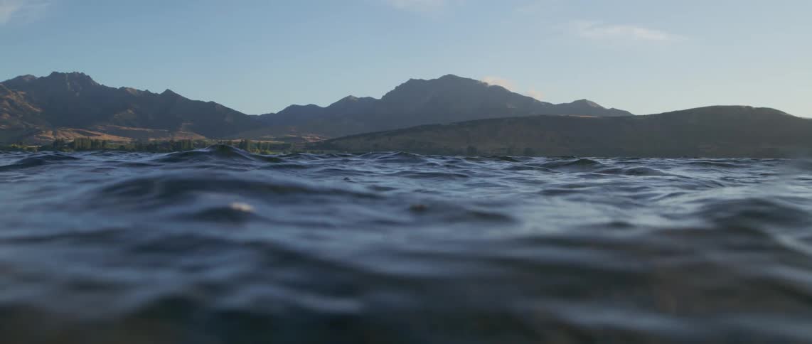 Sunlight shines on the water as it ripples and waves and there are mountains along the coast in the distance