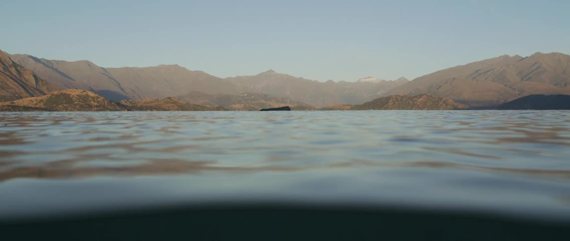 A close up of the surface of water with mountains on the coast line covering the range