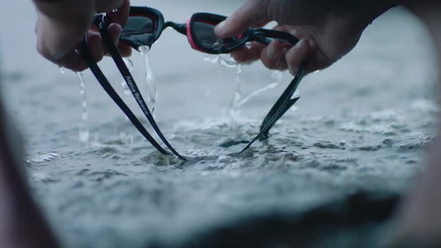 Hands holding swim goggles over light ocean waves and rinsing them in the seawater