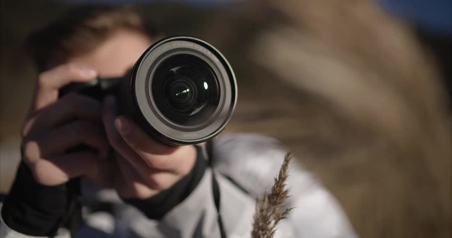 The sun shines on a man as he holds his camera and is looking ahead as he takes a picture