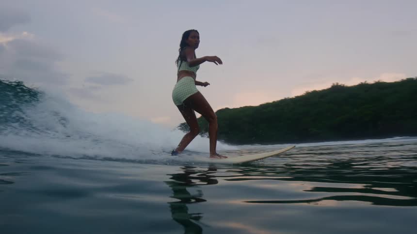 A woman is riding a surfboard during sunset