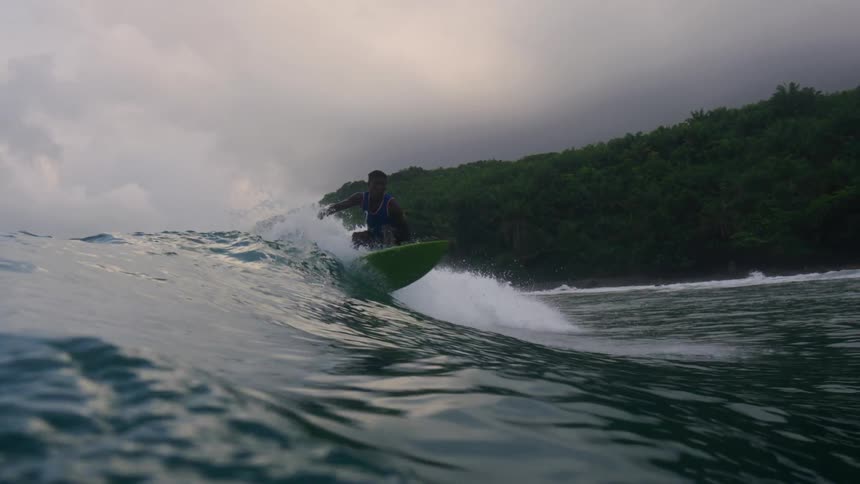 A teenage boy is standing on his surfboard as he rides a wave into shore