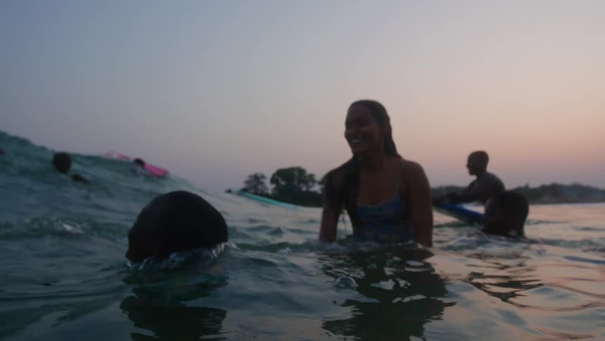 Group of happy friends floating on surfboards dive under a wave at evening