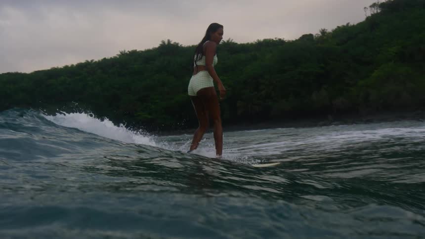A teenage girl is standing on her surfboard as she rides a wave into shore