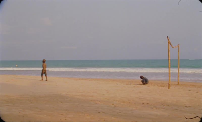 Two young boys stand and crouch on the beach