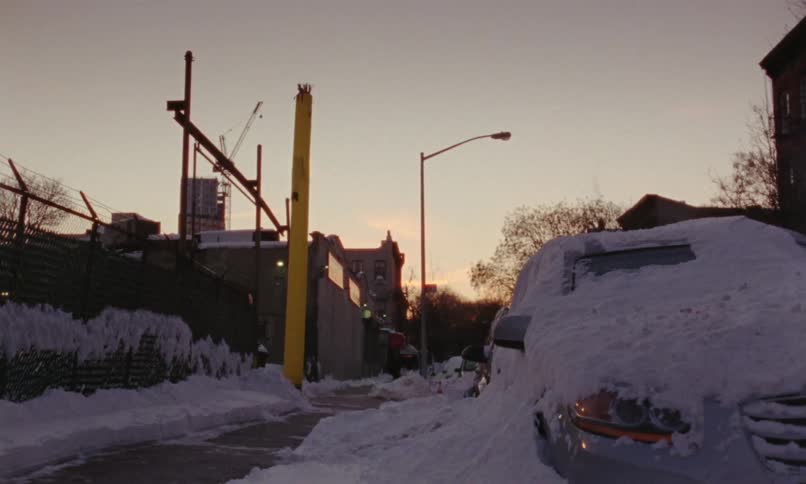 A snow covered car next to a city sidewalk with a yellow up figure near the sidewalk