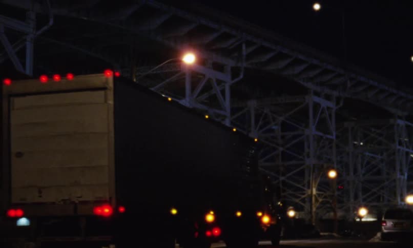 A truck drives down a snow street with a framework of girders in the background