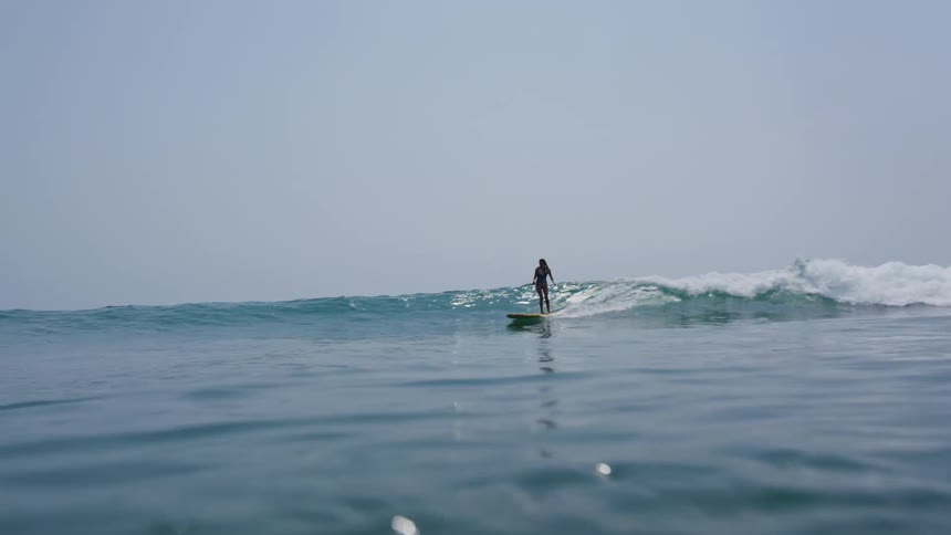 A woman is surfing on ocean water at midday