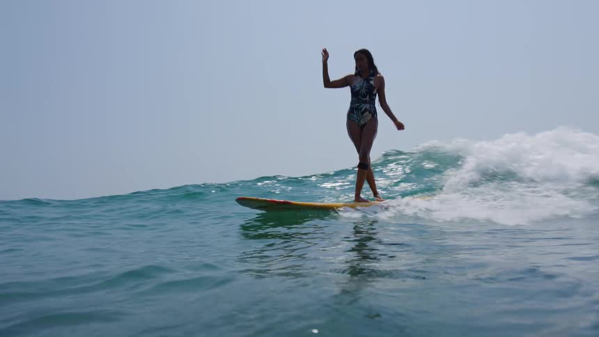 A young woman is balancing on her board while surfing a wave on a bright sunny day