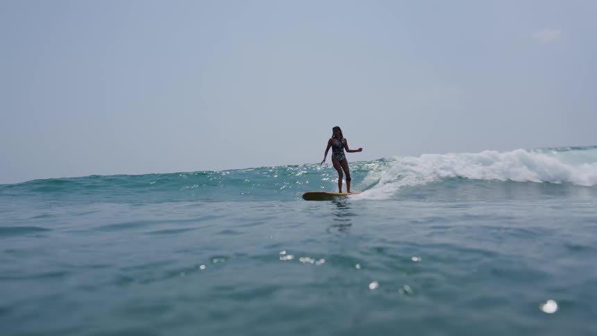 Woman in swimsuit rides on wave on surfboard