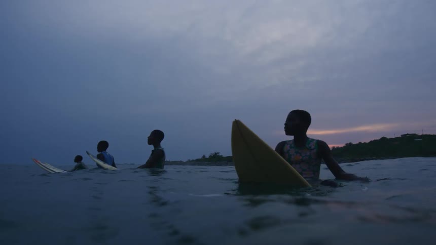 A small group of boys on surfboards bobbing in the ocean at dusk