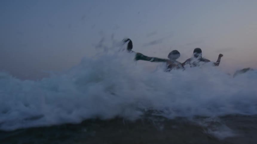 Three teenagers are walking into the water at the beach as waves splash on them