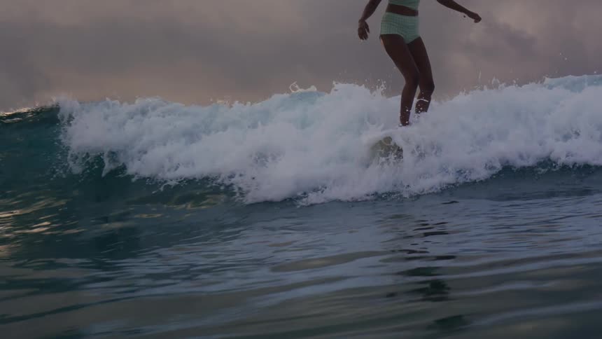 Water splashes as a teenage girl stands on her surfboard and rides a wave