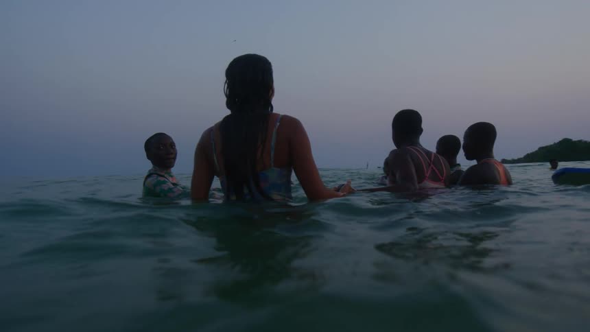 Group of happy friends floating on surfboards dive under a wave at evening