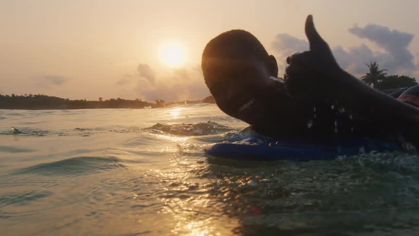 A boy is surfing in ocean water during sunset