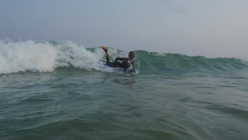 A young boy laying on a surfboard riding it through ocean waves as he rides towards shore