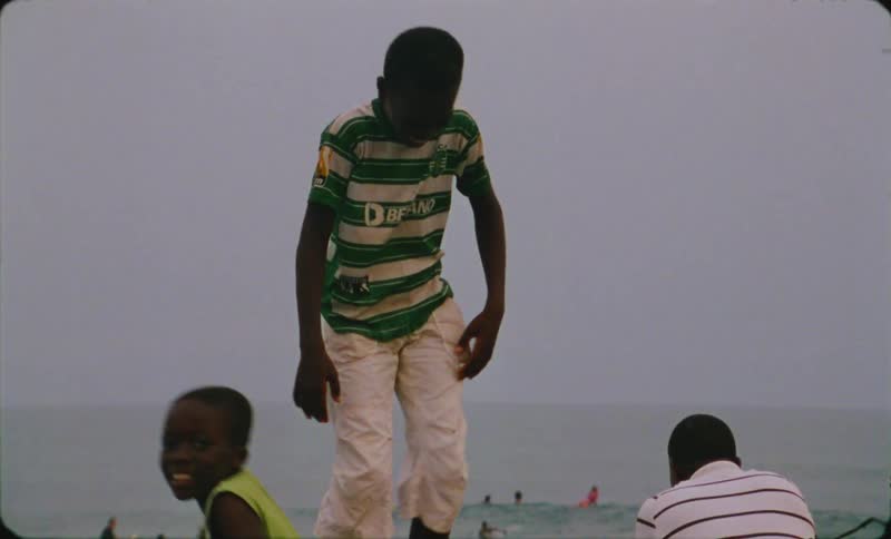 A young boy is playing and dancing on a large boulder with ocean waves behind him