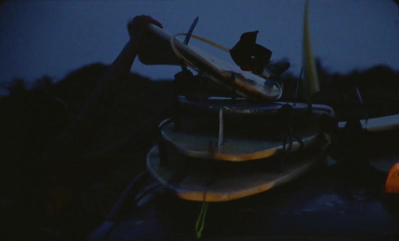 Surfer stacks another board on stack of surfboards on roof of taxi at night