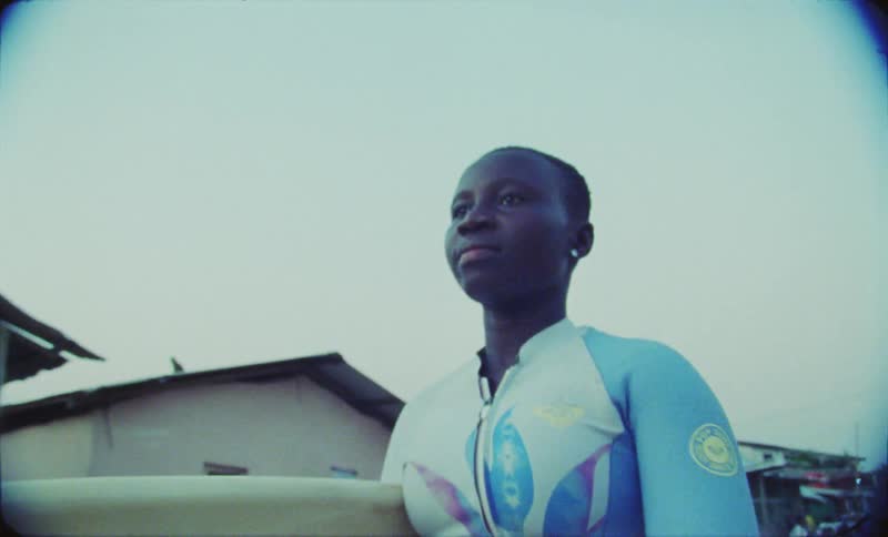 Female surfer carrying surfboard walks along road past houses