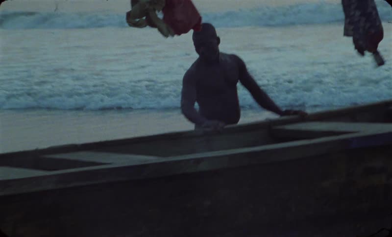 A group of men push a wooden boat toward the ocean