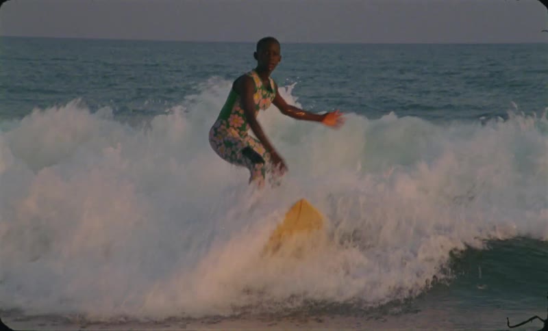 A woman surfing in front of a wave falls off her surfboard and into the ocean