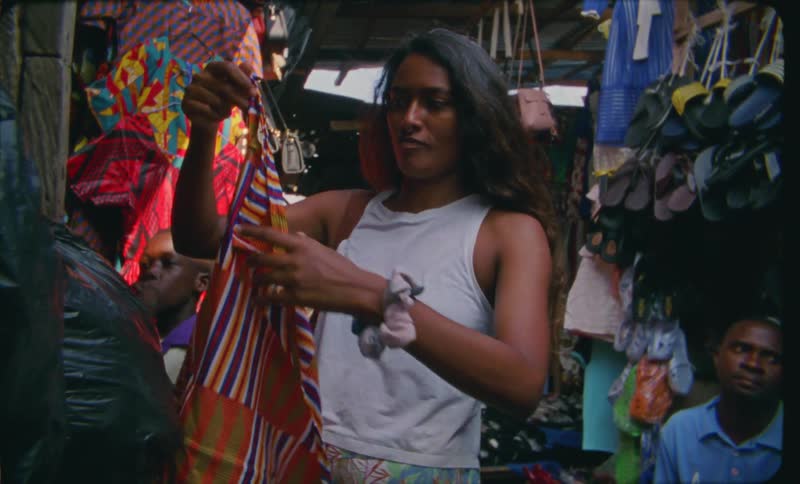 A woman shops for a colorful shirt wrap while the store owner sits and watches