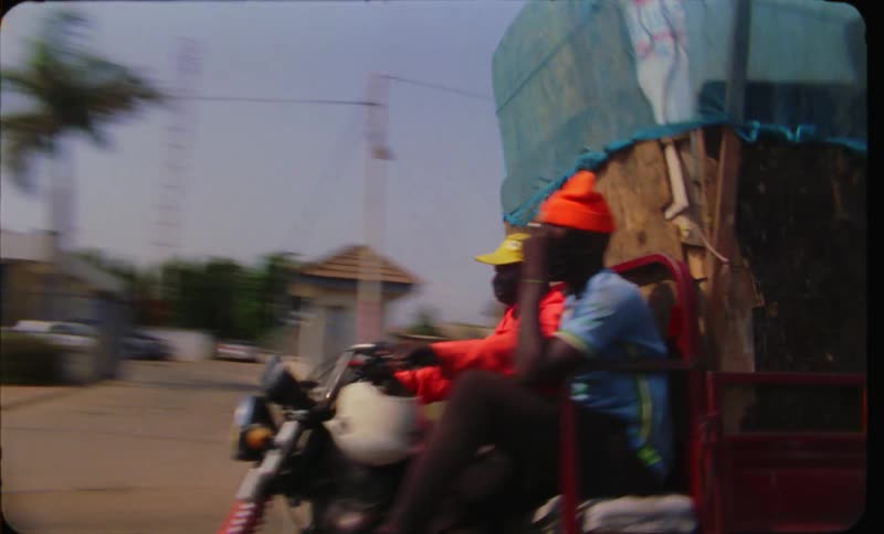 A cargo motorcycle transporting crates moves down a thirdworld urban street