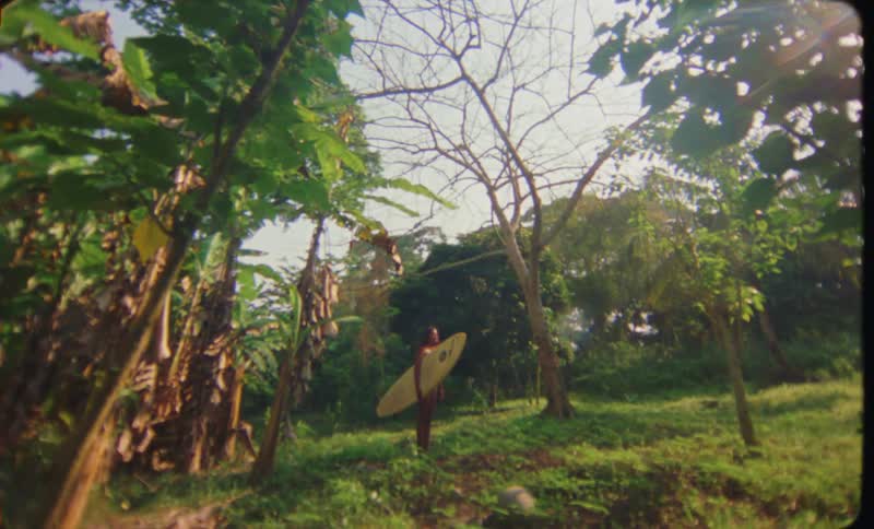 A woman is standing with a surfboard in a wooded area