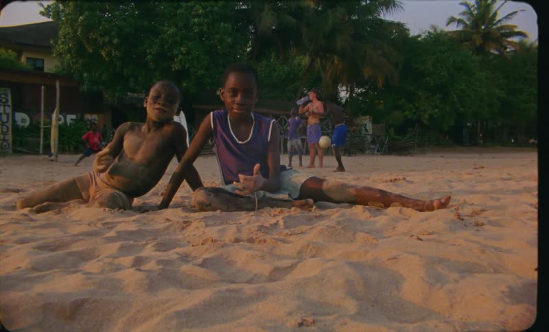 Two boys sitting on sandy beach look at camera