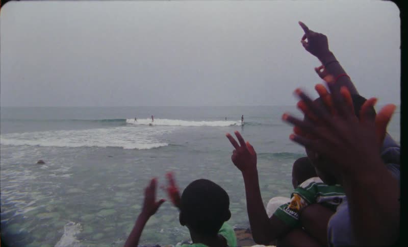 A group of boys cheer while watching surfers on the coast