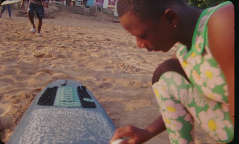 Teenage girl on beach waxing surfboard on the sand