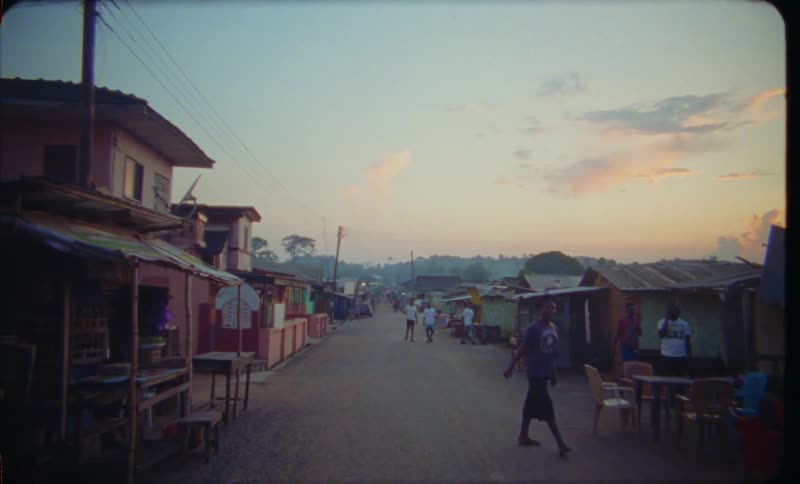Man runs through town as others walk along road with hills in the background