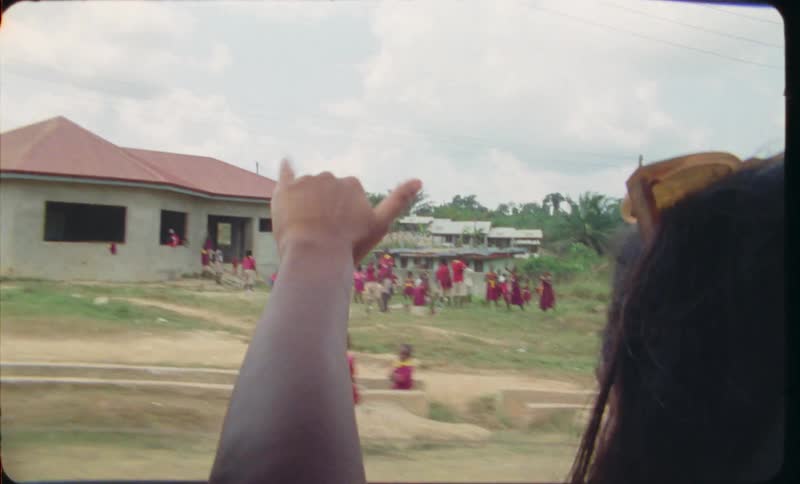 A teenage girl in the back seat of a car waving goodbye and hang 10to a group of kids while driving away