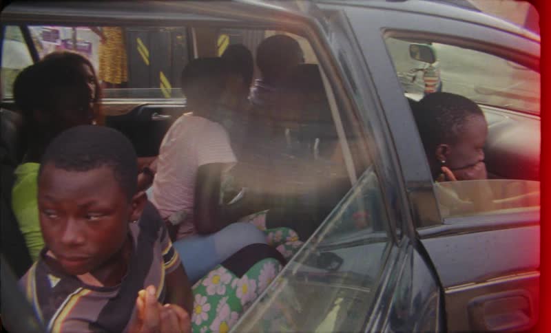 A group of kids piled into a car with surfboards strapped to the roof getting ready to go surfing