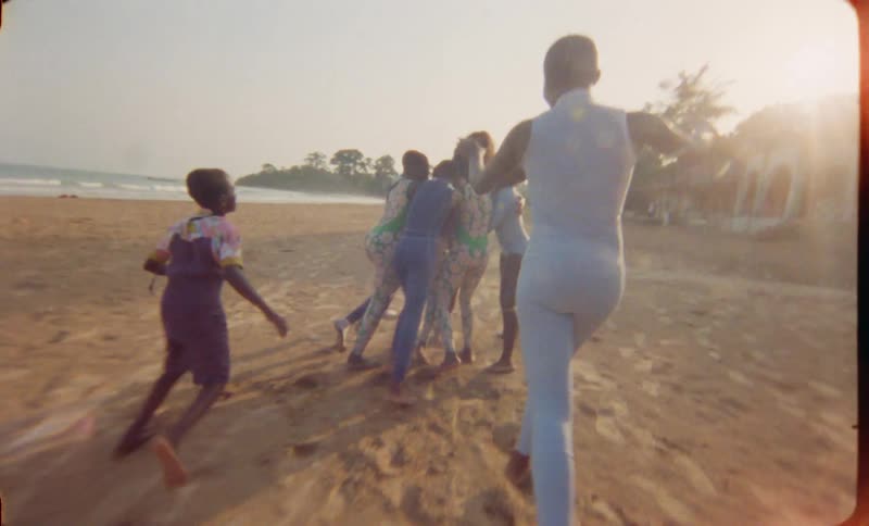 Youths run across beach to hug woman with large building in the background