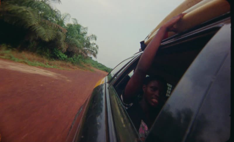 Woman with black shirt sits in the back of car driving on dirt road