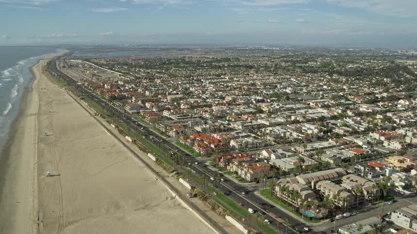 Flying over a partly cloudy Huntington Beach California showcasing coastal roads highways and beachfront residences with the majestic ocean as a backdrop