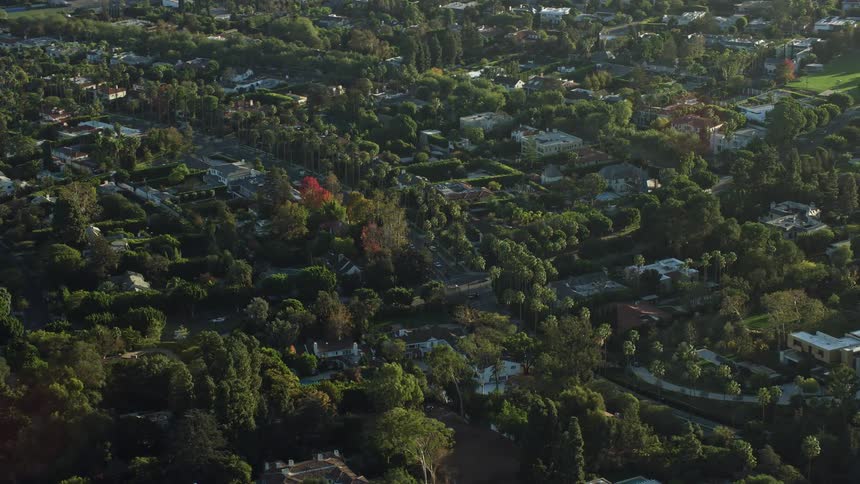 Aerial footage flying by luxurious mansions in Beverly Hills during a sunny day with palm trees and upscale homes