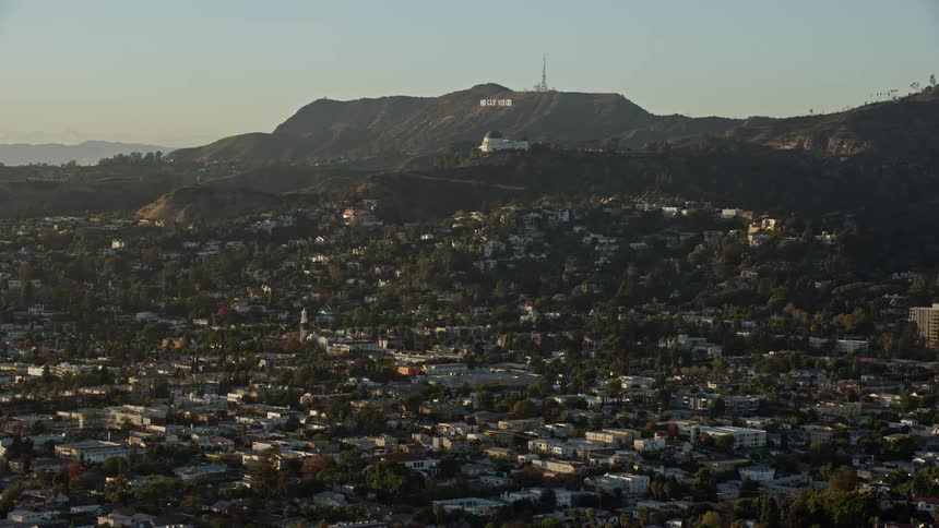 Aerial footage flying over Los Felix to approach the Hollywood sign and Griffith Observatory in Los Angeles California on a partly cloudy day in spring or summer