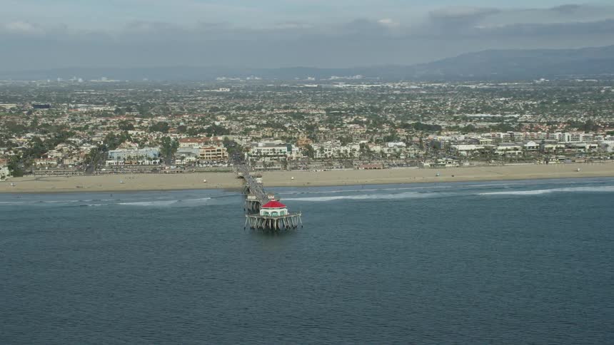 Aerial footage capturing the bustling beach Huntington Beach Pier and the restaurants and residences that line the shore in Huntington Beach California