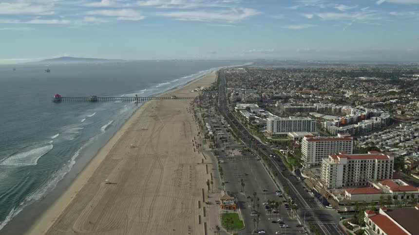 Aerial footage of Huntington Beach Pier and Hyatt Regency hotels in Huntington Beach California on a partly cloudy day during summer