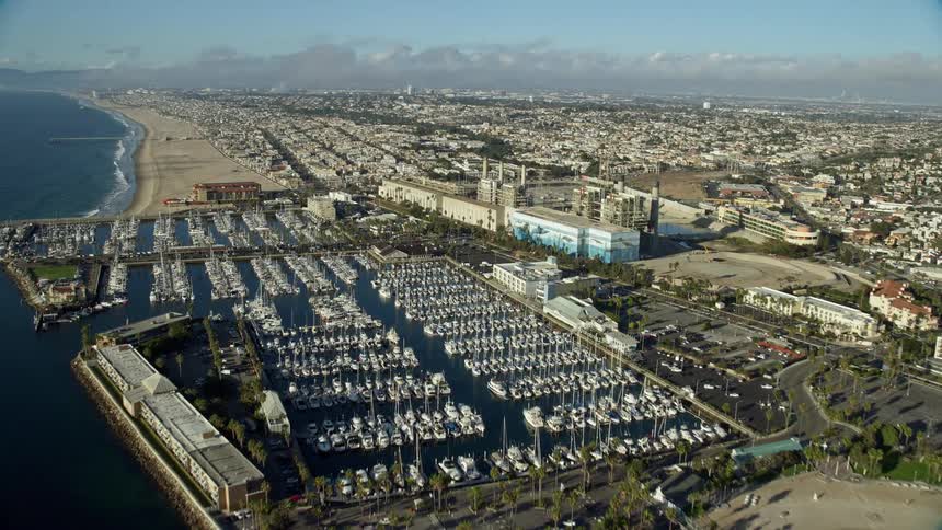 A stunning aerial footage of Redondo Beach California and King Harbor Marina during a partly cloudy day approaching from the seaside