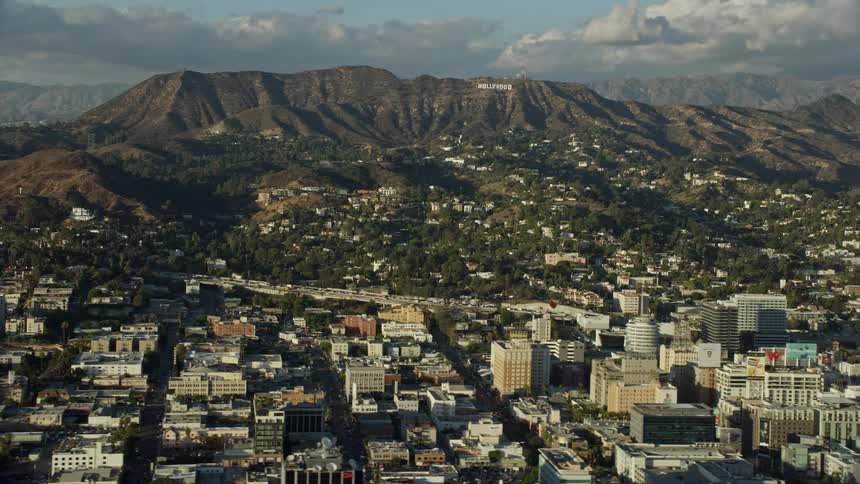 Aerial footage of Hollywood Sign hillside homes and office buildings in Southern California with sunshine and a side view