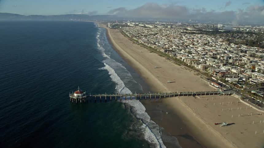Aerial view of Manhattan Beach Pier and surrounding beachside neighborhoods in Southern California during partly cloudy skies