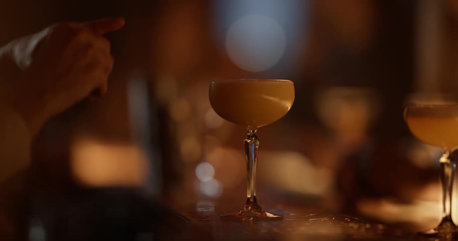 A mixologist sprays a fruit essence over a cocktail at a bar