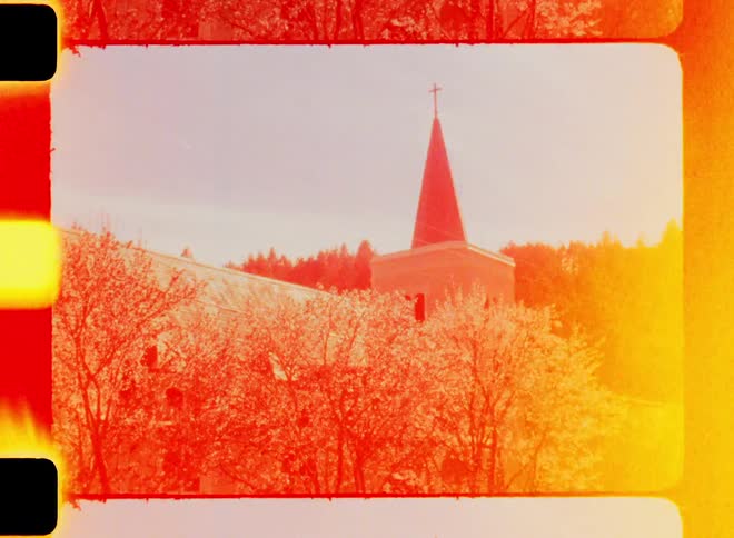 Film footage shows a tall steeple with a cross atop it towering over blooming trees