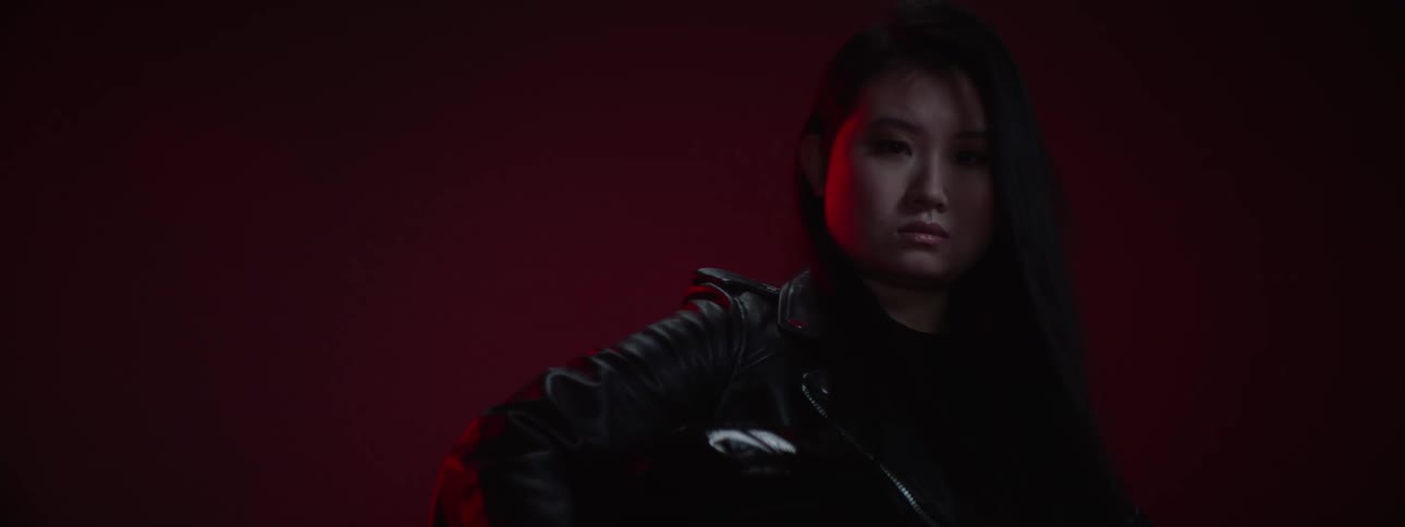 A woman in a leather jacket on a black motorcycle looking sternly