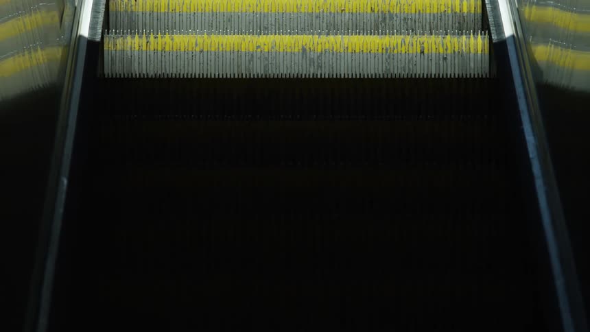 A close up of an escalator displaying steps with yellow paint on them