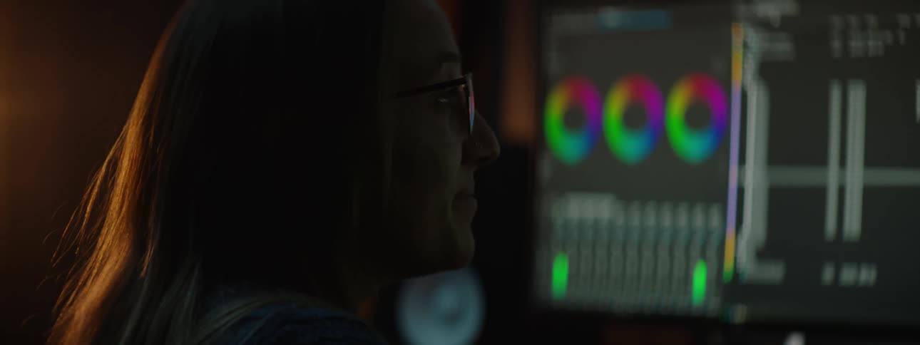 Woman with brown hair and glasses works on computer in dim lit room