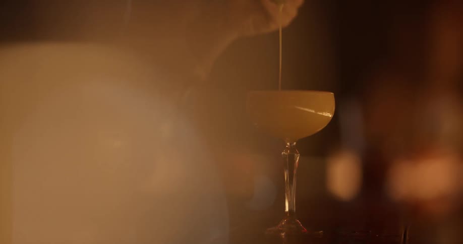 A bartender strains a liquid into a glass